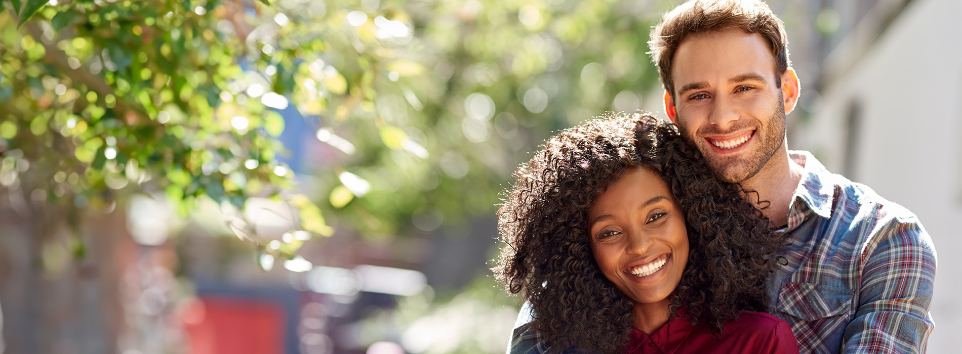 The image shows a man and woman posing for a photo outdoors, with the woman standing slightly behind the man.