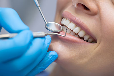 The image depicts a person receiving dental care, with a dental hygienist holding a mirror and cleaning the teeth while the patient is wearing protective gloves.