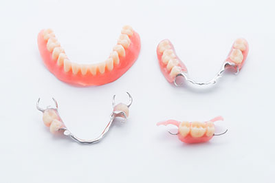 The image shows a set of dentures with visible teeth and gum-like structures displayed in a clear, plastic tray.