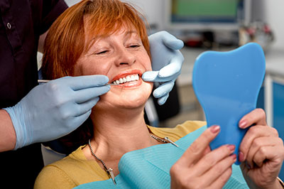 The image shows a woman seated in a dental chair, receiving dental care with a smile on her face.