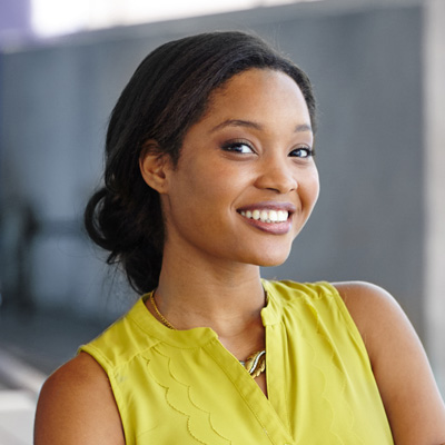 A smiling woman with a confident expression, wearing a yellow top and posing for the photograph.