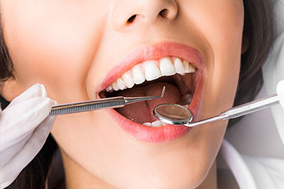 A woman with a broad smile, wearing a medical mask and holding dental instruments in her mouth.