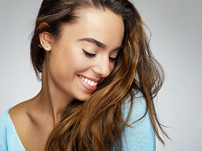 A young woman with long brown hair, wearing a light blue top, smiling and looking to the side.