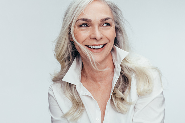 A woman with short blonde hair is smiling and looking towards the camera, wearing a white shirt.