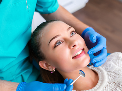 A dental hygienist is performing a teeth cleaning procedure on a patient with blue eyes.